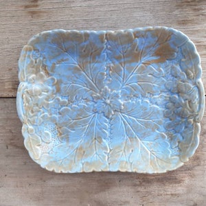 Op de afbeelding: Een lichtblauwe keramische serveerschaal met een reliëf van bladeren. De schaal heeft een rechthoekige vorm met afgeronde hoeken.