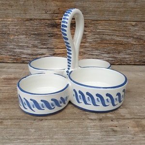May include: A white ceramic condiment holder with four individual bowls and a handle. The bowls have a blue and white wavy pattern.