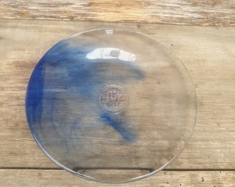 Op de afbeelding: Een heldere glazen plaat met een blauwe swirl-ontwerp en de tekst "Kosta Boda" aan de bovenkant.