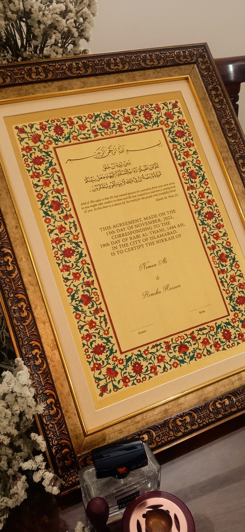 Puede incluir: Un documento enmarcado con un marco dorado ornamentado y un borde floral. El documento es un certificado de matrimonio con texto &aacute;rabe y los nombres "Noman Ali" y "Rimsha Hassan" en la parte inferior.