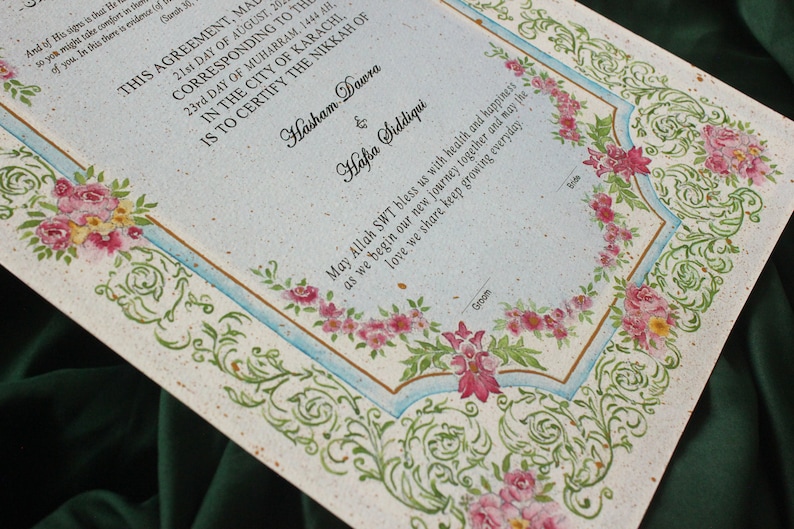 Puede incluir: Un certificado de matrimonio blanco y azul con un borde floral. El texto dice "Este acuerdo hecho el 21 de agosto de 20... correspondiente al 23 d&iacute;a de Muharram, 1444 AH. En la ciudad de Karachi, certifica el Nikkah de Hasham Dawra & Hafsa Siddiqui. Que Allah SWT nos bendiga con salud y felicidad al comenzar nuestro nuevo viaje juntos y que el amor que compartimos siga creciendo cada d&iacute;a."