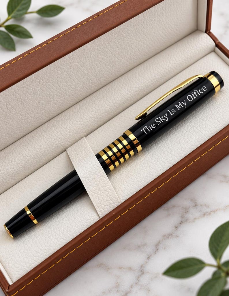 May include: A black and gold ballpoint pen with a gold clip and a decorative gold-banded grip section. The pen is engraved with the text "The Sky Is My Office" and is presented inside a brown rectangular case with a cream-colored interior.