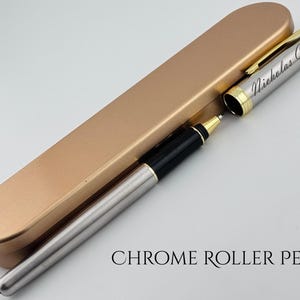 May include: A chrome roller pen with a gold-colored cap and trim, and a matching pen case. The pen is silver with black accents and the name "Nicholas Curro" is engraved on the side. The text "CHROME ROLLER PEN" is below the pen.