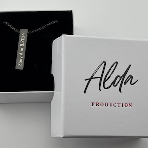 May include: A silver bar necklace with the inscription "Zoey Ann 8.20.14" inside a black box. The box is inside a white box with the word "Alda" in black script and "PRODUCTION" in red.
