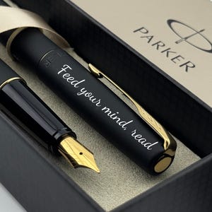 May include: A black Parker fountain pen and pen case set. The pen has a gold nib and clip, and the pen case is black with a beige interior. The pen is engraved with the words "Feed your mind, read".