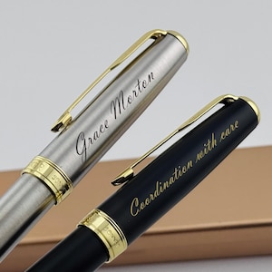 May include: Two elegant pens with gold accents. One pen is silver with the name "Grace Morton" engraved. The other pen is black with the phrase "Coordination with care" engraved. Both pens have gold clips and trim.