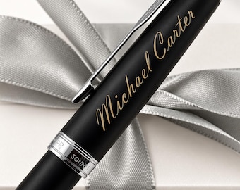May include: A matte black fountain pen with a silver clip and trim. The name Michael Carter is engraved in gold script on the barrel. A silver band near the cap is engraved with the text PARKER SONNET. The pen has a sleek, cylindrical design.