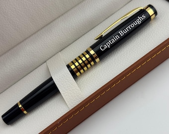 May include: A black and gold pen with the text "Captain Burroughs" in white lettering. The pen is in a white leatherette case with a brown leatherette trim.