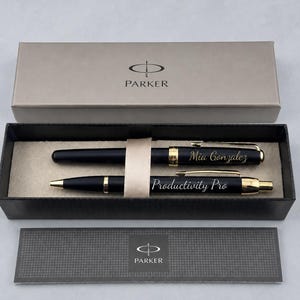 May include: A Parker pen set in a black gift box with a beige interior. The set includes two matte black pens with gold-tone accents. One pen is engraved with the name Mia Gonzalez, and the other is engraved with the text Productivity Pro.
