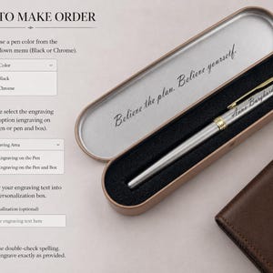 May include: A silver pen with gold accents, engraved with the name "Anna Burghardt," rests in an open, metallic pen case. The case is lined with black velvet and features the inscription "Believe the plan. Believe yourself." A brown leather wallet is next to the pen case.