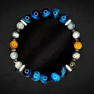 Puede incluir: Una pulsera circular de cuentas con una secuencia de cuentas esf&eacute;ricas pulidas en colores azul, gris y &aacute;mbar. El dise&ntilde;o incorpora peque&ntilde;os espaciadores cil&iacute;ndricos blancos planos y diminutos acentos met&aacute;licos oscuros entre las cuentas.