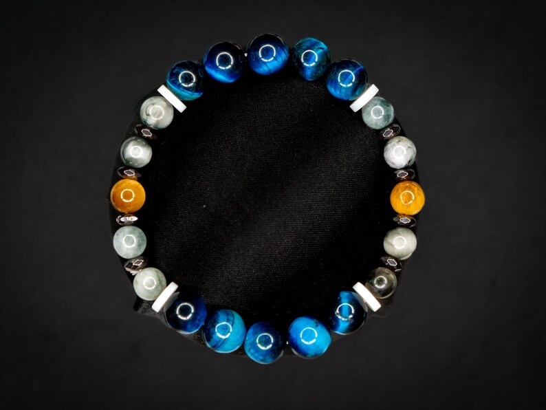 Puede incluir: Una pulsera circular de cuentas con una secuencia de cuentas esf&eacute;ricas pulidas en colores azul, gris y &aacute;mbar. El dise&ntilde;o incorpora peque&ntilde;os espaciadores cil&iacute;ndricos blancos planos y diminutos acentos met&aacute;licos oscuros entre las cuentas.