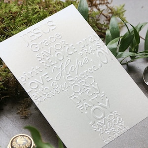 May include: A white card with a cross made of embossed words, including "Jesus", "Grace", "Savior", "Love", "Hope", "Faith", "Pray", and "Salvation".