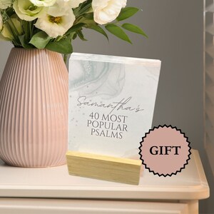 May include: A white card with a marble design and the text "Samantha's 40 Most Popular Psalms" on a wooden stand. A pink sticker with the word "GIFT" is on the table next to the card.