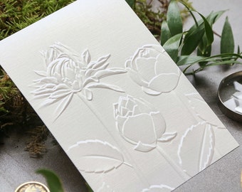 May include: White card with an embossed design of three white flowers. The flowers are stylized and have a delicate, elegant look.