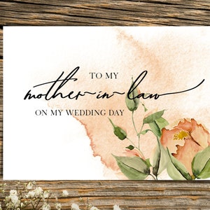 May include: A white card with the text "To my mother-in-law on my wedding day" in black script. The card has a watercolor background with peach and green floral accents.