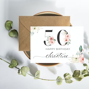 May include: A white card with a floral design featuring the number 50 in black with pink flowers. The text "Happy Birthday Christine" is written in black cursive.