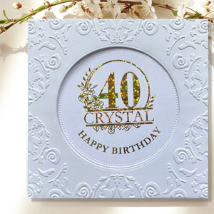 May include: A light blue square greeting card with embossed floral patterns. The center circle features the number "40" in gold with colorful star accents, the name "CRYSTAL", and the words "HAPPY BIRTHDAY".