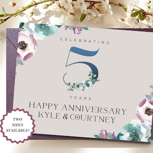 May include: A light gray anniversary card with floral accents. The card reads "Celebrating 5 Years Happy Anniversary Kyle & Courtney." The number 5 is in a blue font with floral embellishments. A small, purple, circular tag reads "Two Sizes Available!"