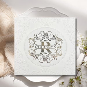 May include: A white card with a gold embossed design featuring a large letter "R" and the name "Robinson" in a decorative font.
