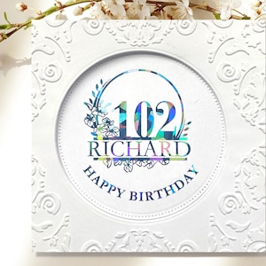 May include: White card with an ornate border and a circle in the center. The circle has a colorful number 102, the name "RICHARD" and the text "HAPPY BIRTHDAY".