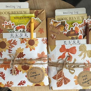 May include: Two wrapped book packages featuring autumn-themed paper with sunflowers and bows, tied with twine. Each includes a Reading Log, Book Review card, Bigelow tea, stickers, a metal paperclip, a pen, and a card labeled CLUE.