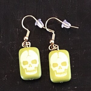May include: A pair of green skull earrings with gold hooks. The skulls are white and have a detailed design.