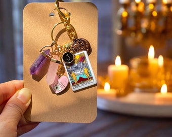 May include: Gold charm keychain with a pink heart, purple crystal, and a tarot card charm that says "The Lovers".