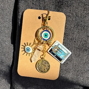 Peut inclure: Porte-cl&eacute;s avec un charme en or, un &oelig;il bleu mal&eacute;fique, un cristal transparent, une carte de tarot avec le texte "La Grande Pr&ecirc;tresse" et un charme de lune en or.