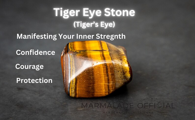 May include: A tiger's eye stone, a brown and gold gemstone with a striated pattern, is shown on a dark gray surface. The text "Tiger Eye Stone (Tiger's Eye)" is above the stone. The text "Manifesting Your Inner Strength" is below the stone. The text "Confidence, Courage, Protection" is below the text "Manifesting Your Inner Strength". The text "MARMALADE OFFICIAL" is below the stone.