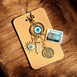 Peut inclure: Porte-cl&eacute;s en or avec un charme &oelig;il bleu mal&eacute;fique, un charme en cristal transparent, un charme soleil avec un &oelig;il, un charme de carte de tarot avec le texte "La Grande Pr&ecirc;tresse" et un charme lune et &eacute;toiles.
