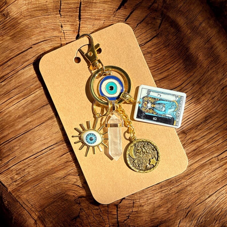 Peut inclure: Porte-cl&eacute;s en or avec un charme &oelig;il bleu mal&eacute;fique, un charme en cristal transparent, un charme soleil avec un &oelig;il, un charme de carte de tarot avec le texte "La Grande Pr&ecirc;tresse" et un charme lune et &eacute;toiles.