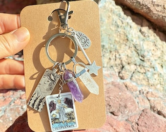 May include: A silver keychain with a variety of charms, including a tarot card with the word "TEMPERANCE", a crystal, a star, and a moon charm.