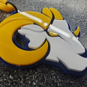 May include: A blue, white, and yellow 3D printed keychain featuring a stylized ram's head with horns.