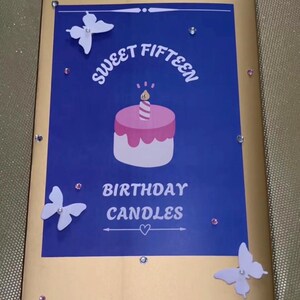 May include: A rectangular gold box featuring a blue center panel with the text Sweet Fifteen Birthday Candles. The design includes a pink cake illustration with a single candle, three white butterfly cutouts, and small clear rhinestones.