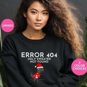 May include: Black sweatshirt with a white graphic that says "ERROR 404 UGLY SWEATER NOT FOUND" and a pixelated dinosaur wearing a Santa hat. The dinosaur is wearing a red and white sweater with snowflakes. The sweatshirt is unisex.