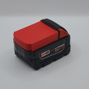 May include: A rectangular power tool battery pack featuring a black base and a bright red top section. The side of the unit displays the text M18 REDLITHIUM XC 5.0 in white and red lettering. The design includes a black release latch mechanism.