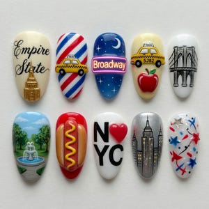 May include: A set of ten artificial nails with various New York City-themed designs. Each nail features unique artwork, including the Empire State Building, a taxi, the Brooklyn Bridge, and the text "Broadway".