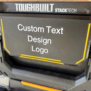 May include: Black and grey Toughbuilt Stacktech tool box with the words "Custom Text Design Logo" in white. The box has yellow accent lines and is designed for hardware storage.