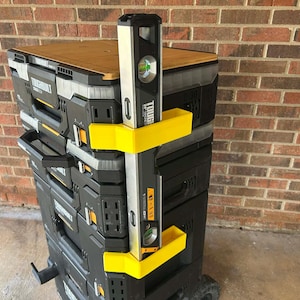May include: A black and yellow rolling tool chest with a wooden top and a level attached. The level is silver and black. The tool chest has multiple drawers and compartments. The level is approximately 60 cm long.