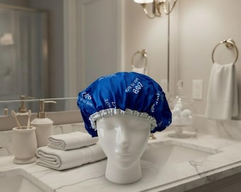 May include: A royal blue shower cap with a white elastic band and a repeating white pattern featuring the Greek letters Zeta Phi Beta and the text Zeta Phi Beta. The shower cap is displayed on a white mannequin head in a bathroom setting.