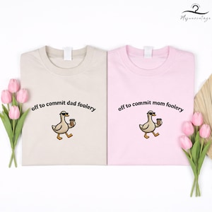 May include: Two t-shirts, one beige and one pink, each with a cartoon duck wearing sunglasses and holding a coffee cup. The beige shirt says "off to commit dad foolery" and the pink shirt says "off to commit mom foolery".