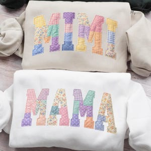 May include: Two sweatshirts, one beige and one white, each with a patchwork design spelling out "MIMI" and "MAMA" in colorful fabric. The letters are in various pastel colors and floral patterns.