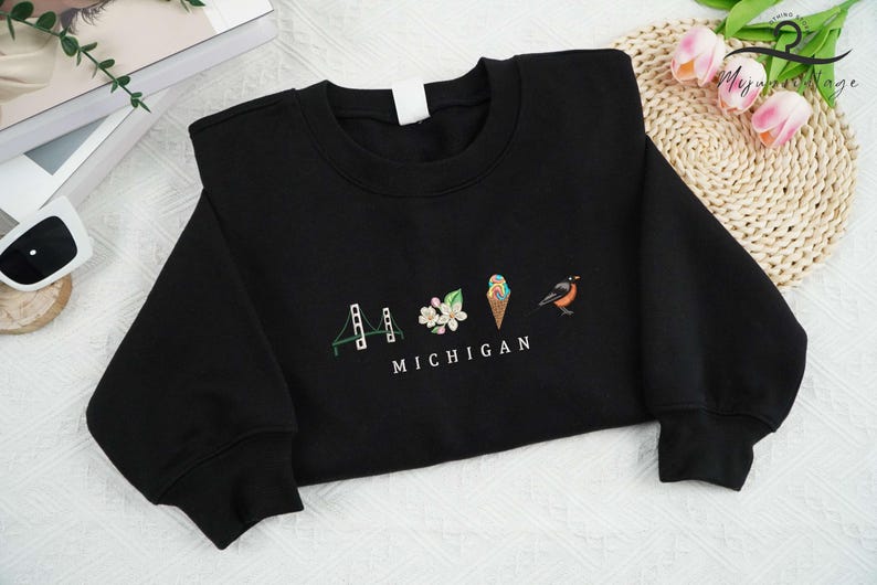 May include: Black sweatshirt with a white graphic design featuring a bridge, a flower, an ice cream cone, and a bird with the text "MICHIGAN".