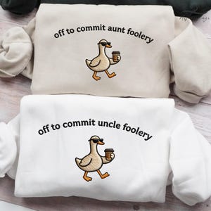 May include: Two sweatshirts, one cream and one white, each with the embroidered phrase "off to commit aunt foolery" and "off to commit uncle foolery". Both sweatshirts feature a cartoon duck wearing sunglasses and holding a coffee cup.