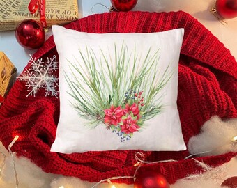 Puede incluir: Un cojín cuadrado blanco con un diseño de acuarela de agujas de pino verdes, flores de pascua rojas y bayas azules. El cojín está sobre una superficie de punto roja, rodeado de adornos navideños, cajas de regalo y luces de hadas.