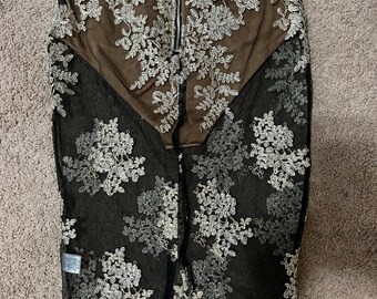 Pode incluir: Saia preta transparente com bordado floral dourado. A saia tem um fecho de correr nas costas.