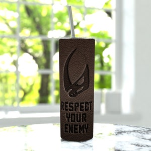 Puede incluir: Un vaso de acero inoxidable marr&oacute;n con una textura de cuero negro y un s&iacute;mbolo mandaloriano. El vaso tiene el texto "Respect Your Enemy" impreso en &eacute;l.