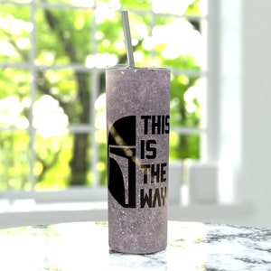 Pode incluir: Um copo de pl&aacute;stico com glitter roxo com um capacete de Mandaloriano preto e o texto "This is the way".