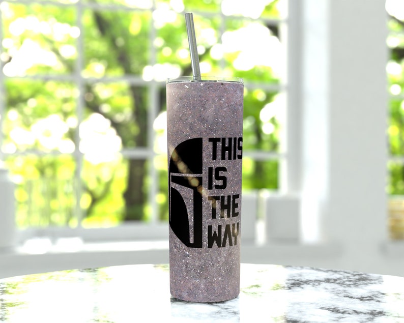 Pode incluir: Um copo de pl&aacute;stico com glitter roxo com um capacete de Mandaloriano preto e o texto "This is the way".